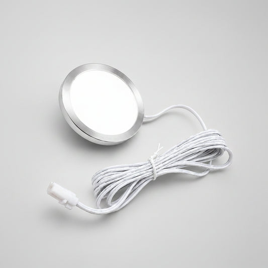 A round silver LED light panel with a white diffuser and a coiled white power cord, shown on a solid beige background.