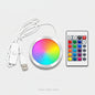 A round RGB LED light strip controller with a white USB cable and a white remote control, displayed on a clean white background.