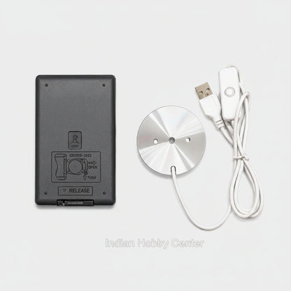 A wireless remote control kit featuring a round brushed silver metal transmitter and a white wired remote with a USB connector, shown next to a black rectangular battery or power unit on a plain white background.