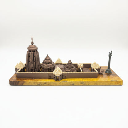 A detailed miniature temple model set on a wooden base, displayed on a dark blue table with office chairs and another model in the background.