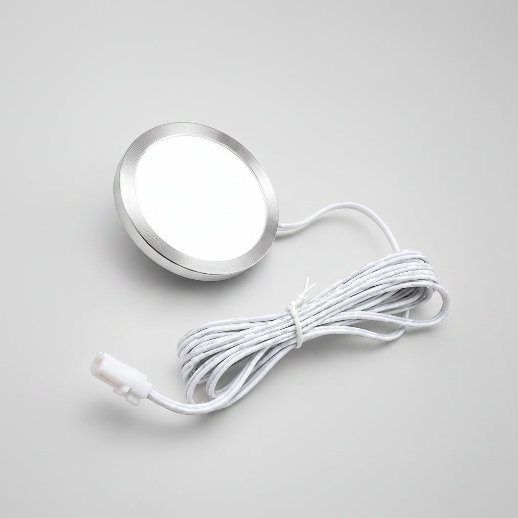 A round silver LED light panel with a white diffuser and a coiled white power cord, shown on a solid beige background.
