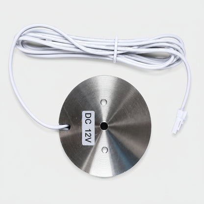 A round brushed-metal sensor module with a white cable and connector, labeled 'DC 12V', on a light gray background.