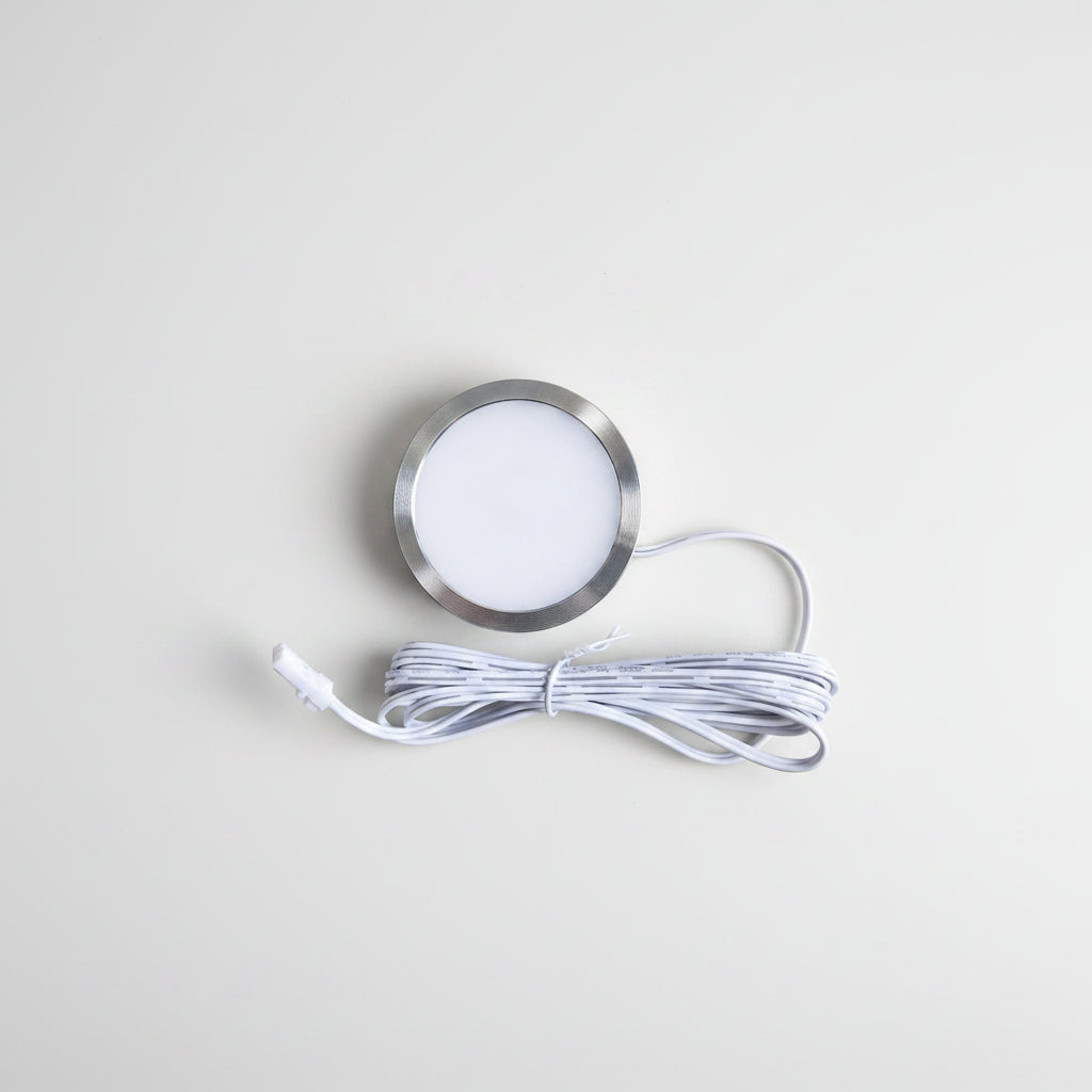 A round recessed LED light fixture with a brushed silver metal rim and a white diffuser, shown with its coiled white power cable on a plain white background.