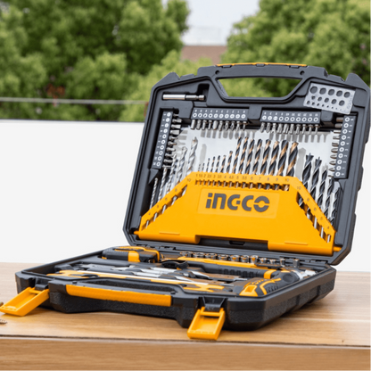 Open tool case with tools and drill bits on a wooden surface, blurred greenery in the background